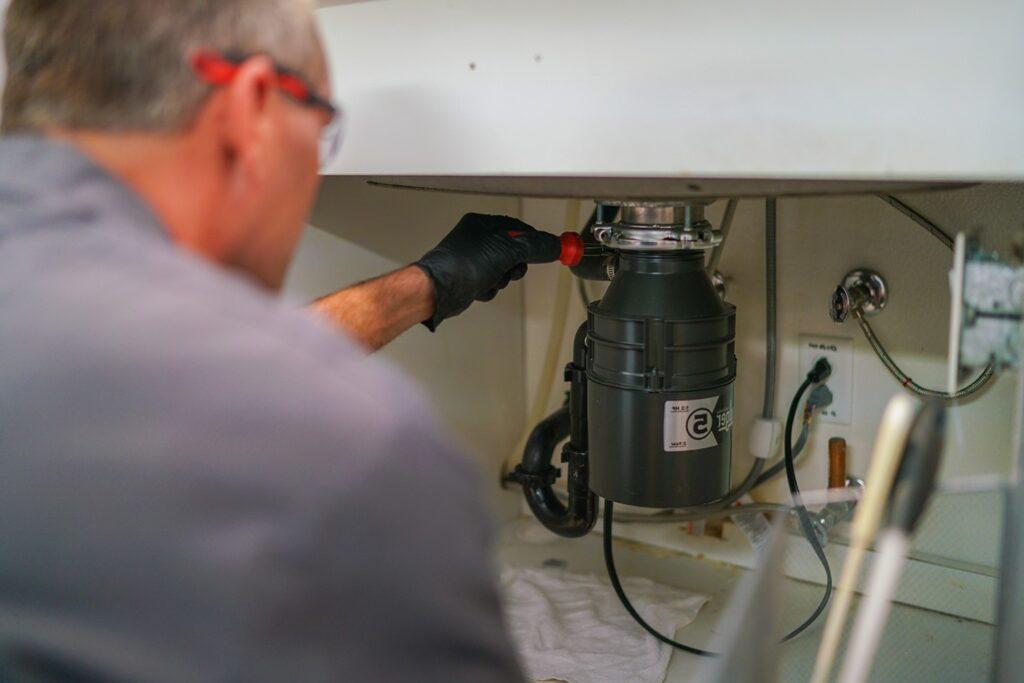 Technician installing a garbage disposal under a kitchen sink in Naperville, IL